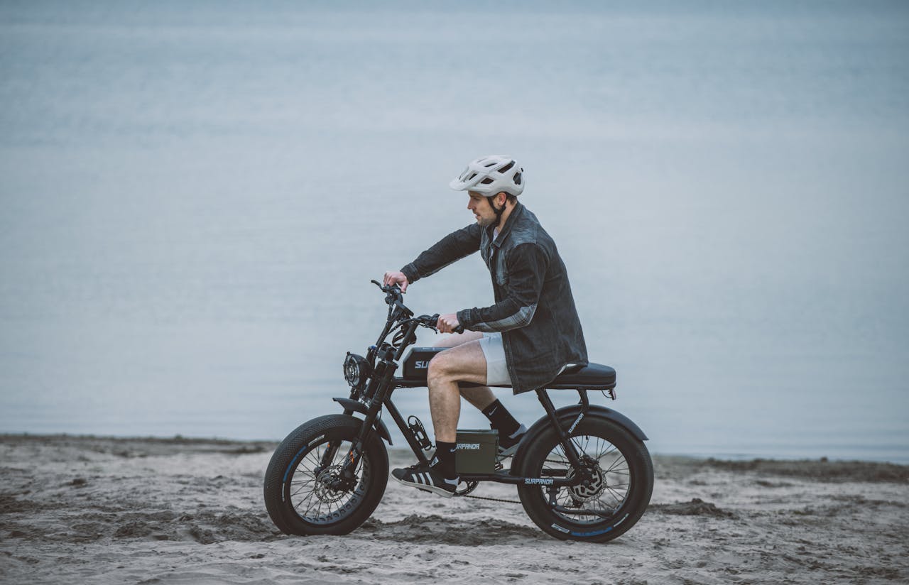 A man wearing a helmet rides an electric bike on a beach, showcasing leisure and outdoor activity.